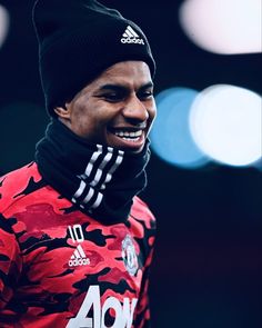 a man wearing a red camo shirt and black beanie smiles at the camera