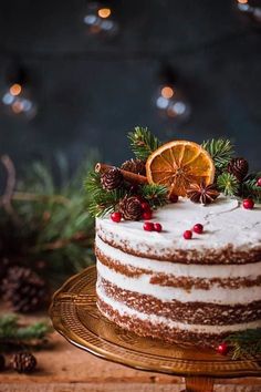 a white cake with orange slices and pine cones on top is sitting on a gold platter