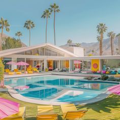 a pool with chairs and umbrellas around it in front of a palm tree covered house