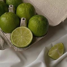 some limes are sitting in a basket on a white table cloth next to a slice of lime