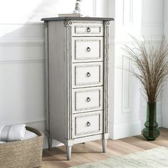 a white dresser with drawers and a basket next to it on the floor in front of a wall