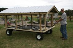 a man standing next to a small chicken coop on top of a trailer in the grass