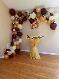 the balloon arch is decorated with gold, white and burgundy balloons that spell out 50