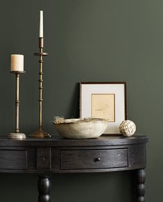 a wooden table with a bowl and candles on it next to a framed photograph, candle holder and other items