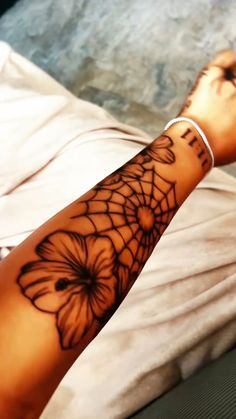 a woman's arm with a spider web and flowers tattoo design on the wrist