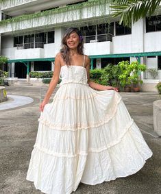 a woman standing in front of a building wearing a white dress with tiered ruffles