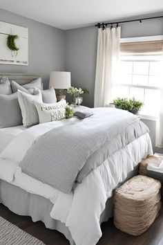 a bed with white sheets and pillows in a bedroom next to a window filled with potted plants