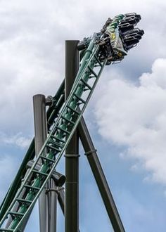 a roller coaster going down the side of a tall metal structure in front of a cloudy blue sky