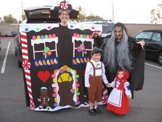 two adults and one child are standing in front of a large gingerbread house costume