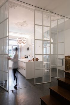 a woman is walking through an open room with glass walls and stairs to the kitchen