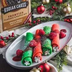 some food is on a white plate with christmas decorations around it and a box of kodia cakes in the background