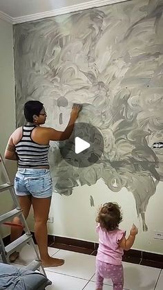 a woman and child are painting a mural on the wall