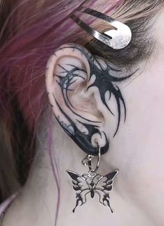 a close up of a person's ear with tattoos on it and a butterfly hanging from the side