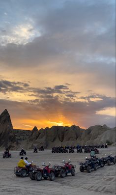 a group of people riding four wheelers on top of a sandy field at sunset