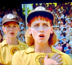 two women in yellow shirts and baseball caps standing next to each other with their mouths open