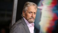 an older man with grey hair wearing a gray suit and pink shirt looking at the camera