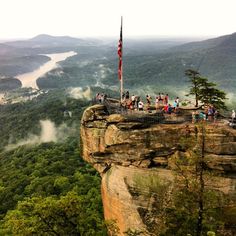 people are standing on the edge of a cliff with a flag flying in the wind