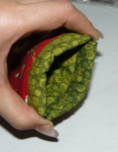 a hand holding a small green and red pouch on top of a white countertop