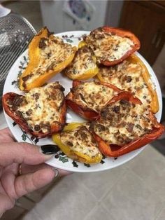 someone holding a plate full of stuffed peppers with cheese on top and seasoning in the middle