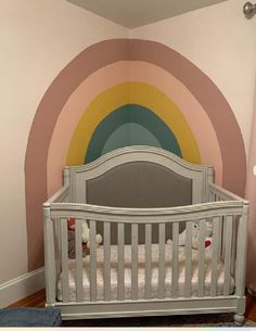 a baby's room with a crib and rainbow painted on the wall