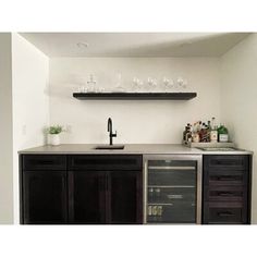 a kitchen with black cabinets and wine glasses on the shelf above the sink is shown