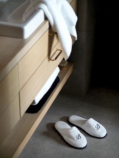 two pairs of slippers sitting on the floor in front of a sink and towel