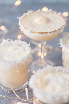 three cocktails with coconut garnish on the rim and two glasses filled with them