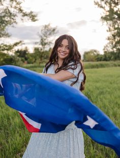 a woman in a white dress is holding a blue flag and smiling at the camera