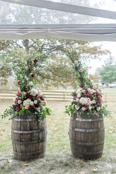 two wooden barrels with flowers and greenery on them are set up for an outdoor ceremony