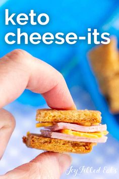 a hand holding a ham and cheese sandwich in front of a blue tray with crackers