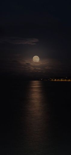 the full moon is seen over the ocean at night with clouds in the sky and water