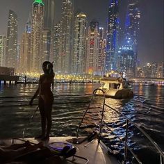 a man standing on the bow of a boat in front of a city skyline at night