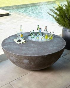 an outdoor table with bottles and glasses on it next to a swimming pool in the background