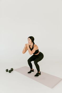 a woman squats on a yoga mat while holding her hands behind her head and looking at the camera