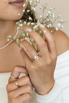 a woman in white dress holding flowers and wearing two gold engagement rings on her finger