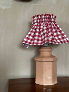 a red and white checkered lamp shade sitting on top of a wooden table next to a clock