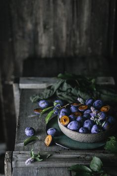 a bowl filled with blueberries sitting on top of a wooden table next to leaves