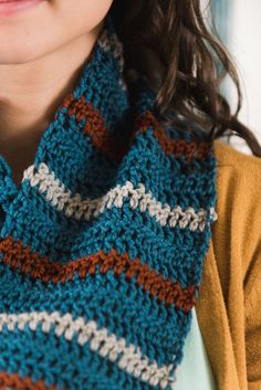 a close up of a woman wearing a blue and brown knitted cowl scarf