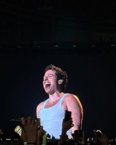 a man in white tank top standing on stage with his mouth open and people holding their hands up