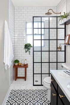 a white tiled bathroom with black and gold accents on the shower door, toilet and sink