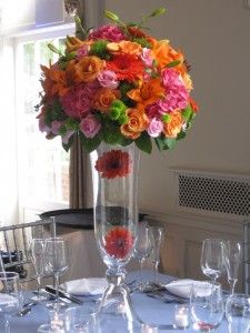 a vase filled with lots of colorful flowers on top of a white table cloth covered table