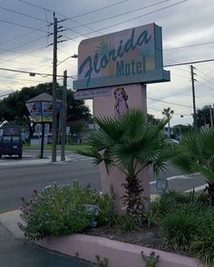 a motel sign sitting on the side of a road next to palm trees and flowers