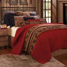 a bed with a red comforter and pillows on it in front of a fireplace