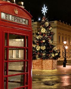 a red phone booth sitting in front of a christmas tree with lights on it's side