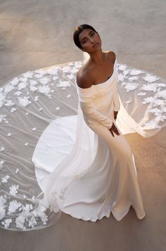 a woman in a white dress is sitting on the sand with her arms behind her back