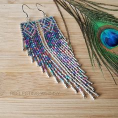 a pair of earrings with beads and feathers on a wooden surface next to it is a peacock feather