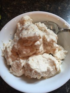 a white bowl filled with mashed potatoes on top of a black counter next to a spoon