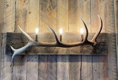 a deer antler is mounted on a wooden wall with three lit candles in it