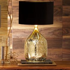 a lamp that is sitting on top of a table next to a book and glass vase