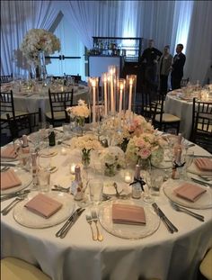 the table is set with many plates and place settings, candles in vases, and flowers